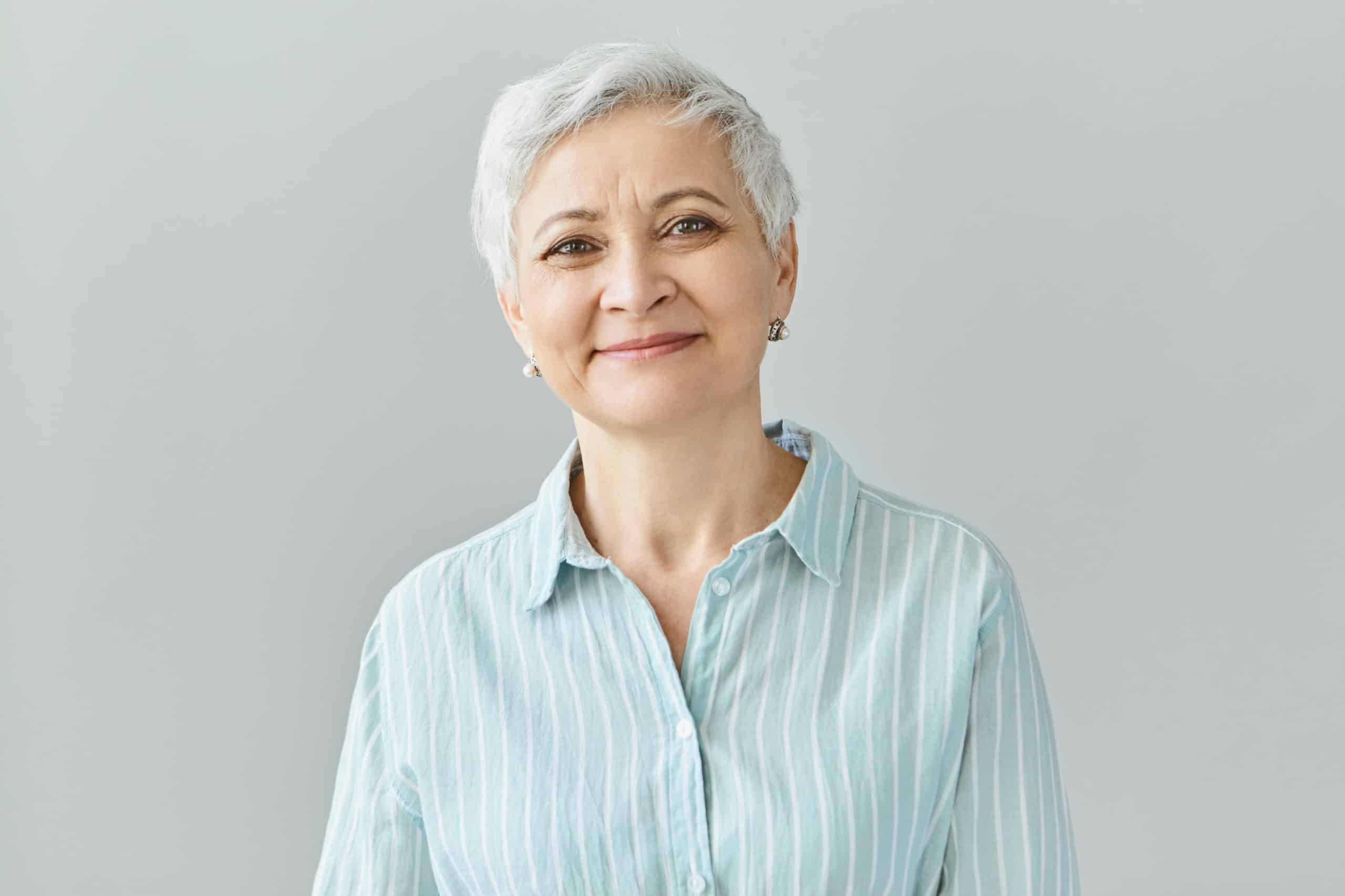 Positive human reactions, feelings and emotions. Charming elegant middle aged sixty year old female with short gray hair looking at camera with pleased smile, her eyes full of happiness and joy