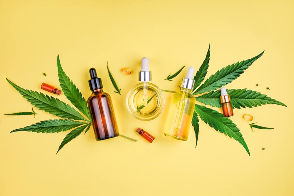 Different glass bottles with CBD OIL, THC tincture and cannabis leaves on yellow background. Flat, minimalism. Cosmetics CBD oil.